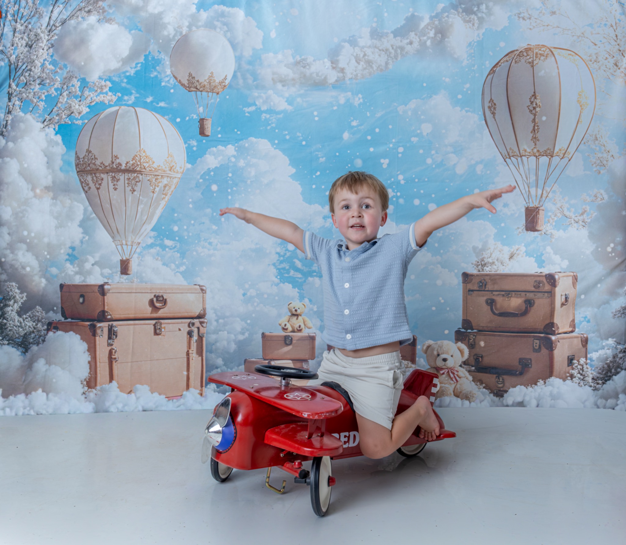 Child stretching both arms out while sitting on a red toy airplane