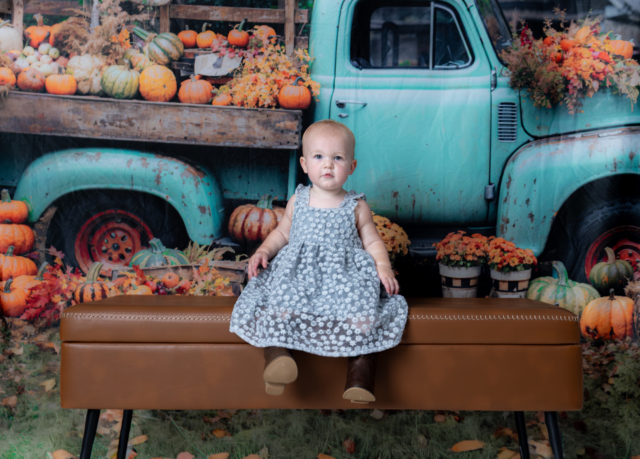 Child sitting on a bench in front of a teal truck and pumpkin backdrop