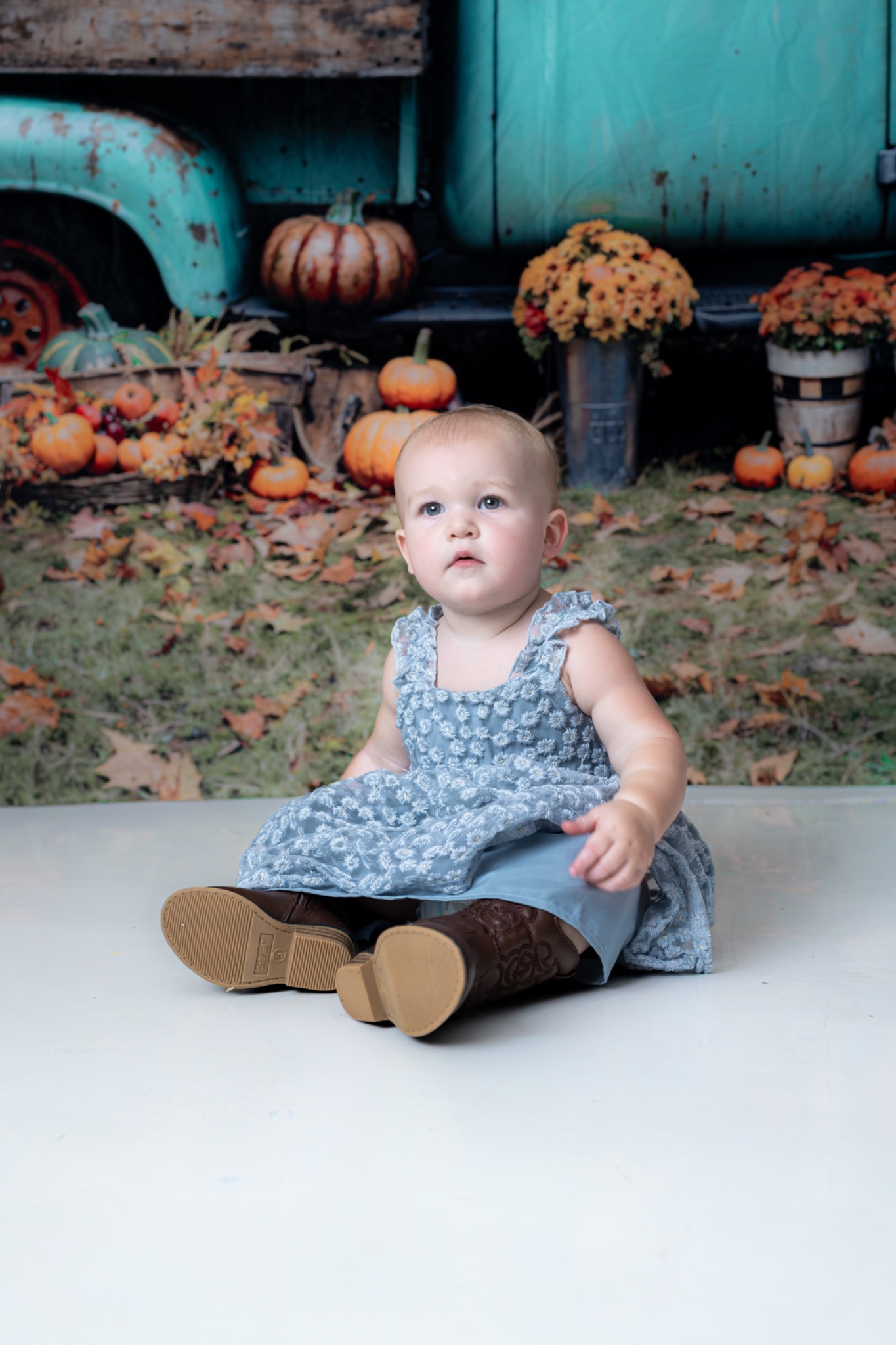Child sitting in a blue dress in front of an autumn backdrop with pumpkins and a teal truck