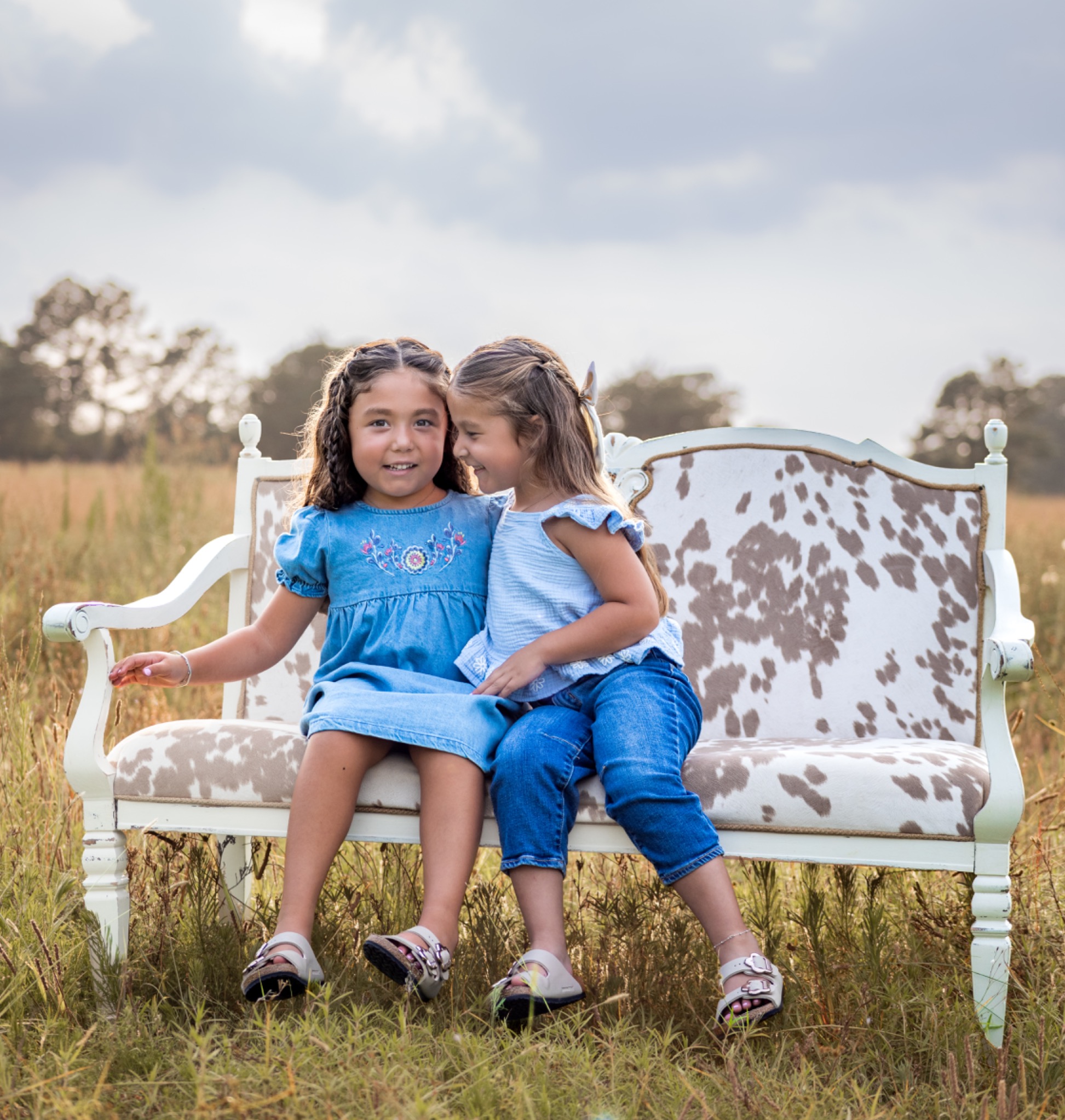 Two children sitting together on a patterned bench in a meadow