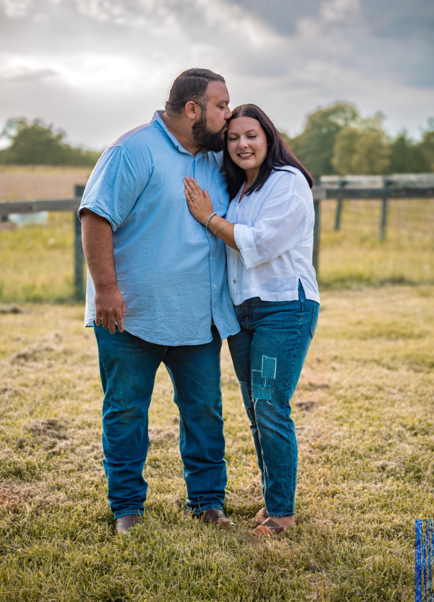 Couple standing close together in a meadow, with one kissing the other on the head