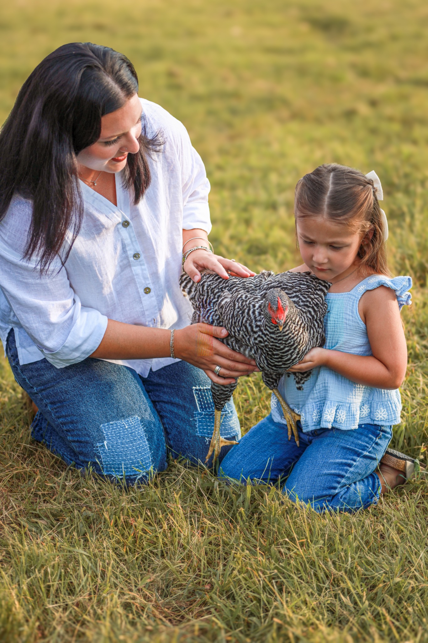 Adult and child holding a barred chicken in a meadow