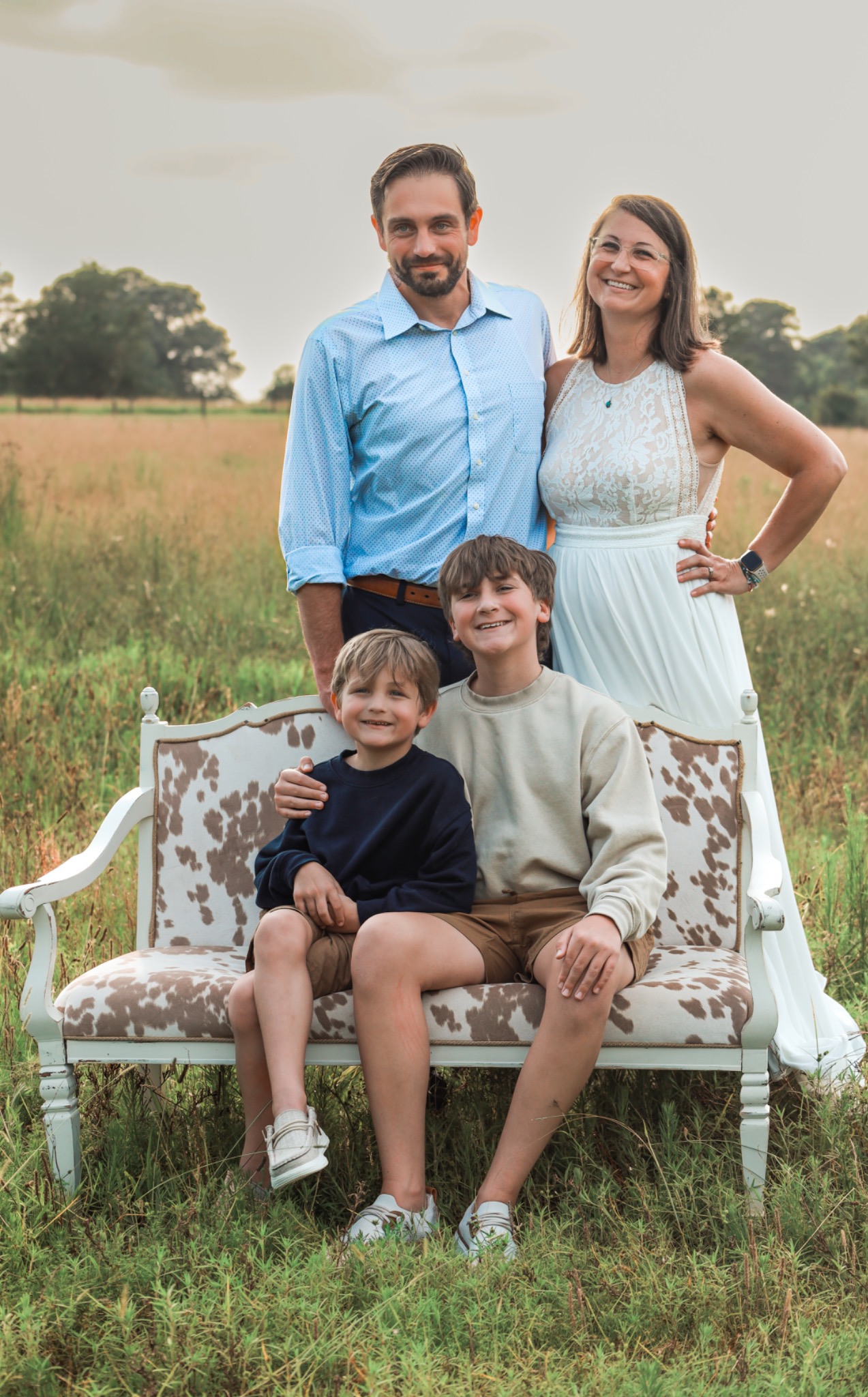 Two adults standing behind two children seated on a patterned bench in a meadow
