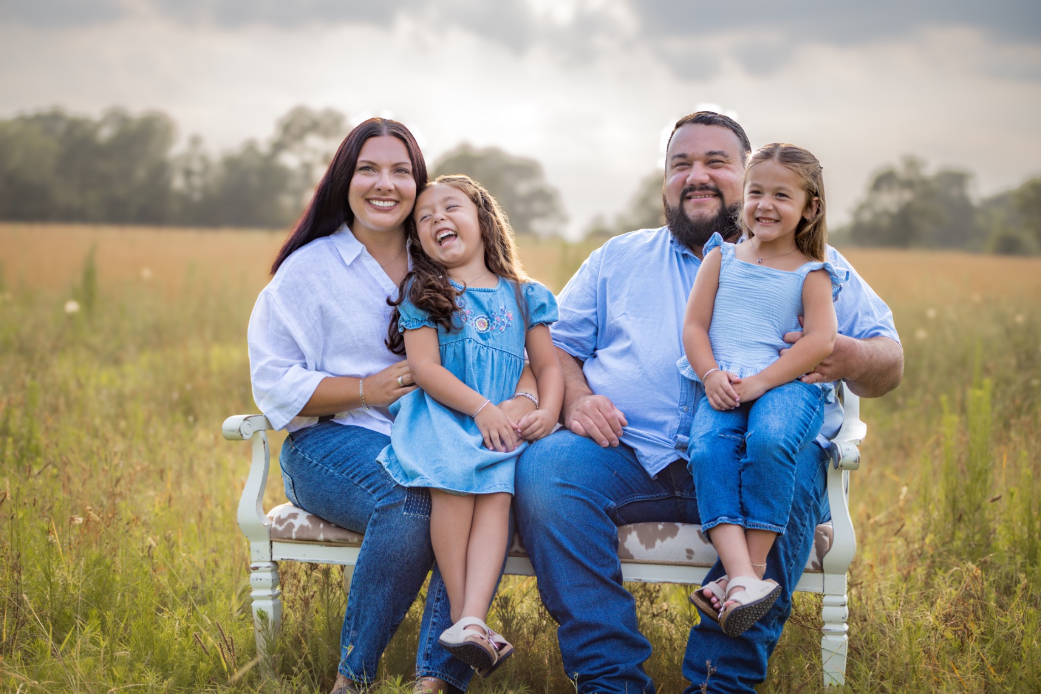 Two adults and two children in blue dresses seated together in a meadow