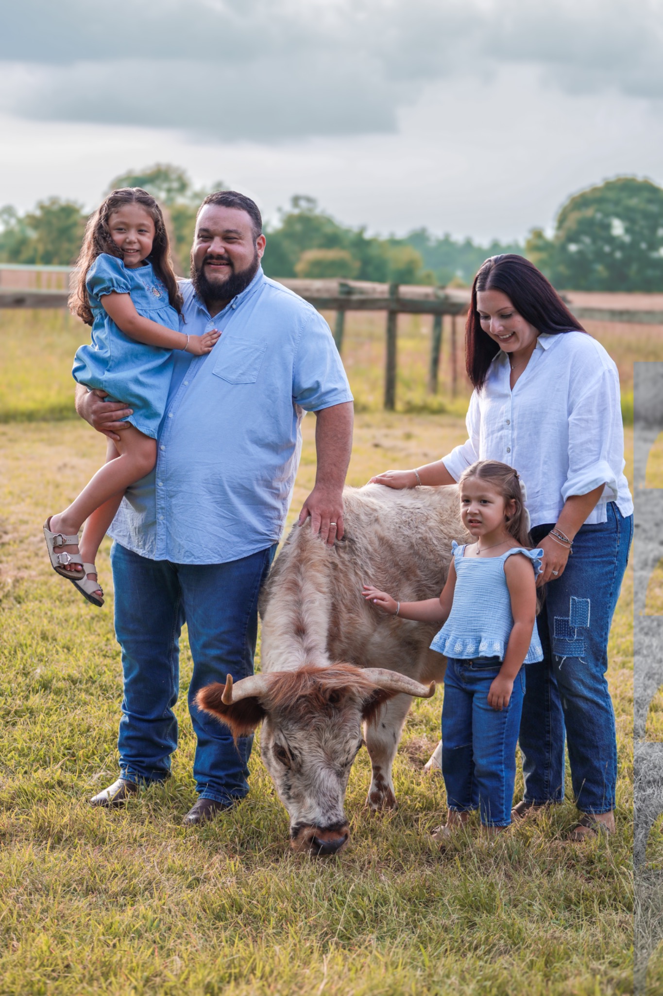Two adults and two children gathered beside a longhorn cow in a pasture
