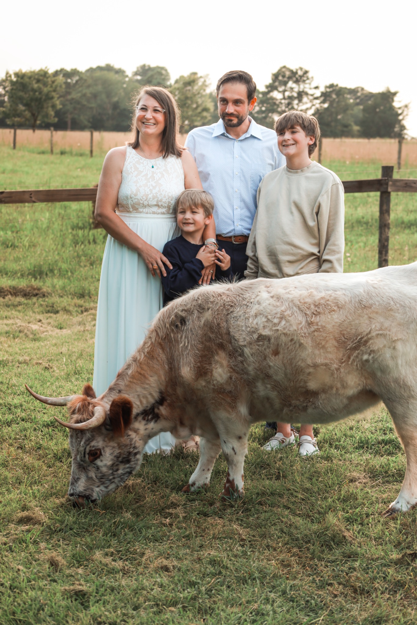 Family standing in a pasture with a longhorn cow in the foreground