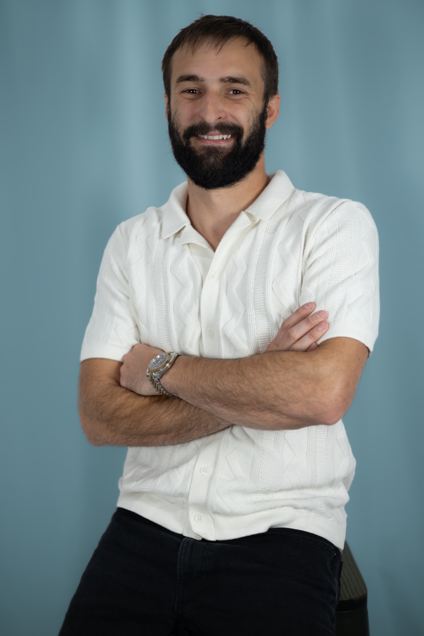 Studio portrait of a smiling bearded man in a white shirt with his arms crossed
