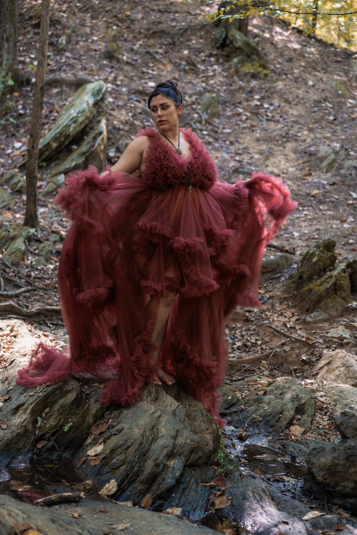 Maternity portrait in a flowing rose-colored gown among woodland rocks