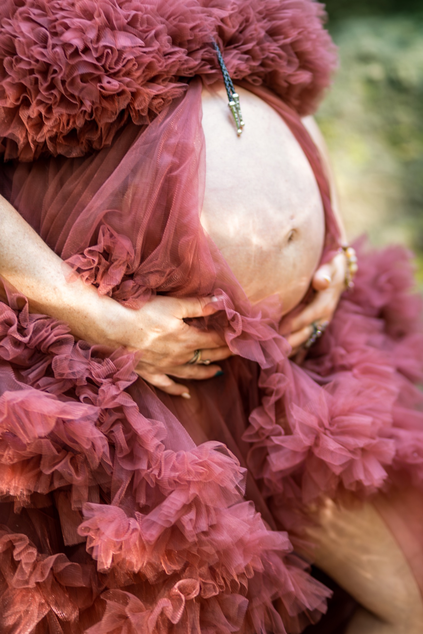Close-up maternity portrait with hands resting on a belly framed by a rose-colored gown
