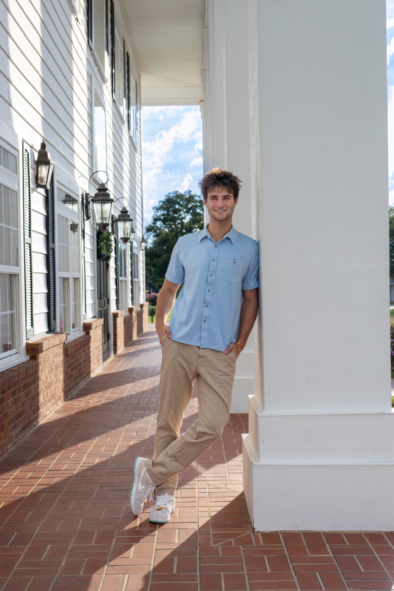 Senior in a light blue shirt leaning against a white column