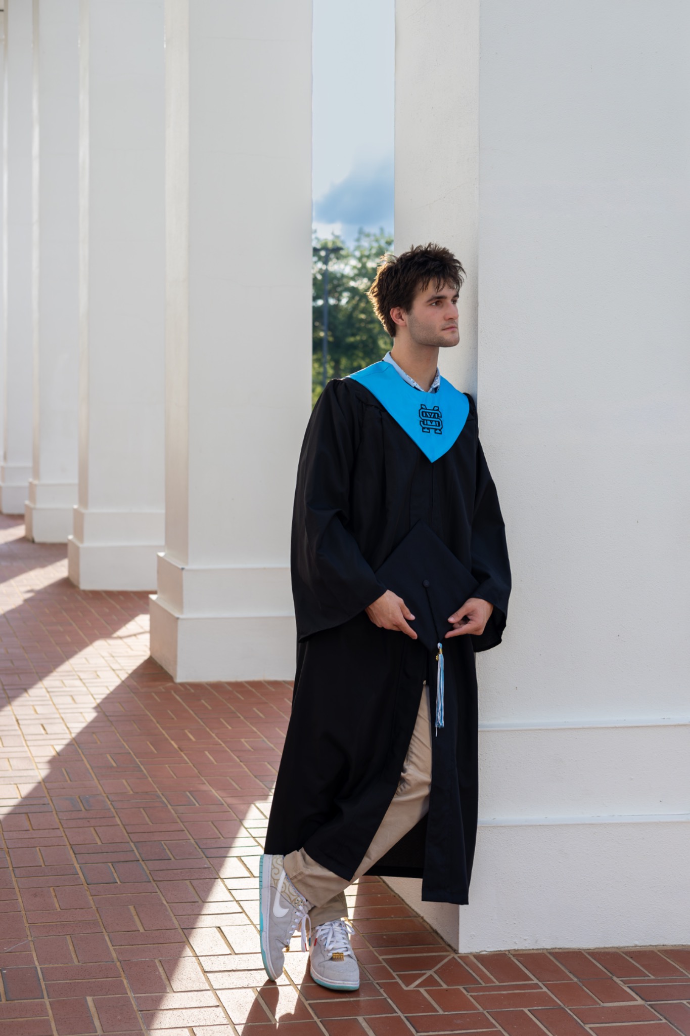 Senior in graduation regalia standing beside white columns